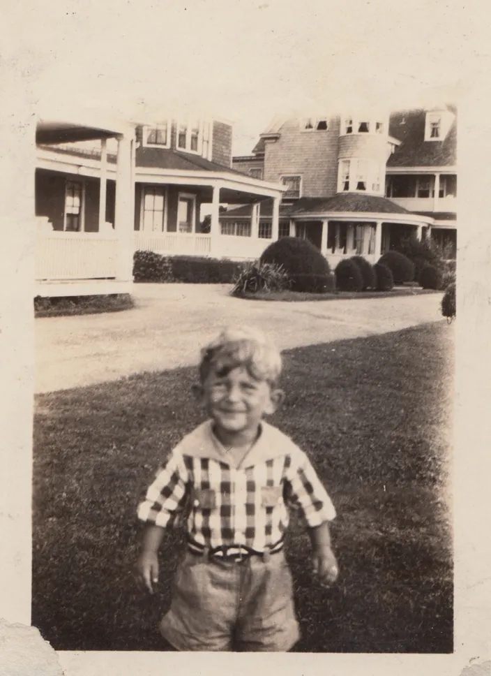 Norman Mailer as a small child, c. 1925, on a lawn before a row of large summer houses