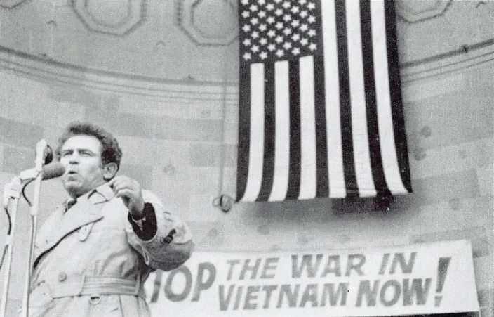 Norman Mailer speaking at an anti-Vietnam War rally beneath a "Stop the War in Vietnam Now!" banner, 1966